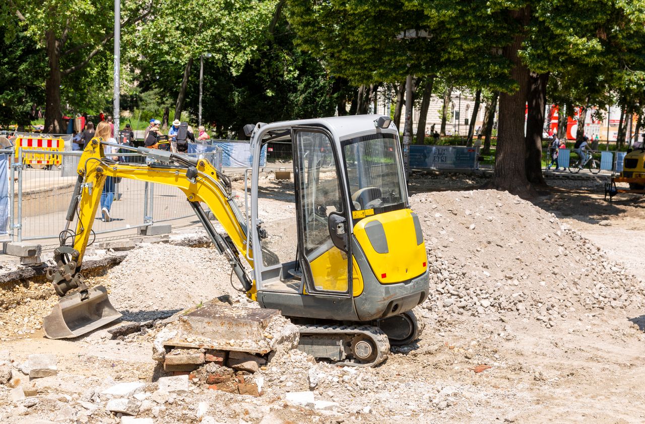 Yellow mini excavator in operation at a busy city construction site during the day.