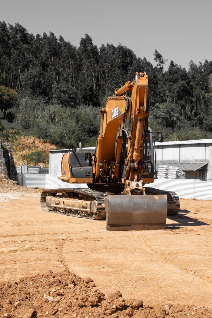 Large orange excavator on a construction site with trees in the background.
